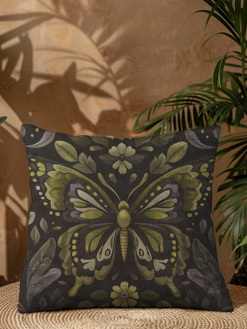 A square decorative pillow featuring an intricately detailed butterfly design in olive green, sage, and cream colors against a black background. The butterfly is surrounded by botanical elements with symmetrical floral patterns.